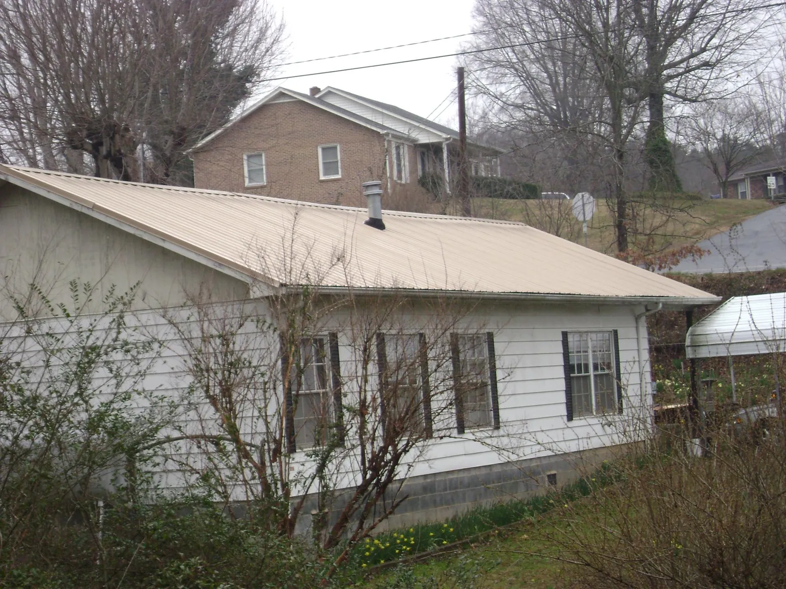Tan metal roof on a white sided house set into a hillside — Commercial Roofing by Roofing Brothers in Pembroke